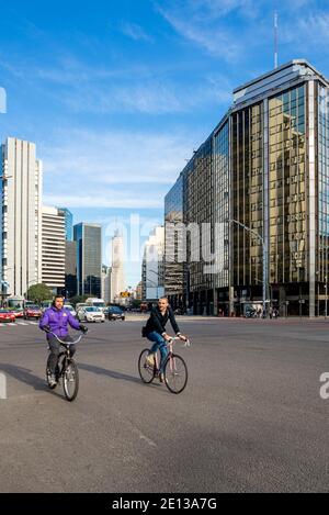 Buenos Aires, Retiro Finanzviertel. Zwei Männer auf dem Fahrrad überqueren eine leere Straße, Geschäftsgebäude im Hintergrund Stockfoto