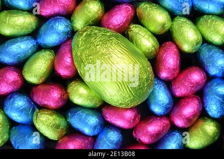 Haufen Gruppe von mehrfarbigen, verschiedenen Größen von bunten Folie verpackt Schokolade ostereier in rosa, blau, gelb und lindengrün mit einem großen Ei. Stockfoto