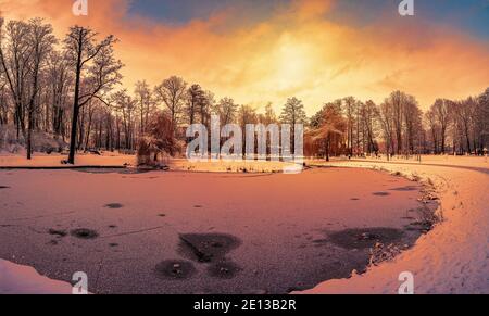 Sonnenuntergang über Park mit kleinem See und mit Schnee bedeckt Bäume Stockfoto