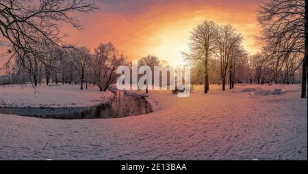 Panoramablick auf den Sonnenuntergang über Park mit kleinem Kanal mit Enten und bedeckt mit Schneebäumen Stockfoto