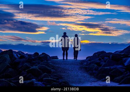 Zwei Frauen gehen bei Sonnenaufgang am New Brighton Beach, Wirral, mit ihren Hunden. Stockfoto