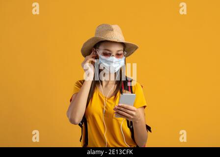 Weibliche Reisende in Gesichtsmaske hören Musik auf dem Smartphone Stockfoto