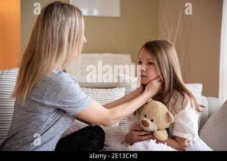 Mama überprüft die Kehle und das Fieber ihrer kranken Tochter. Stockfoto