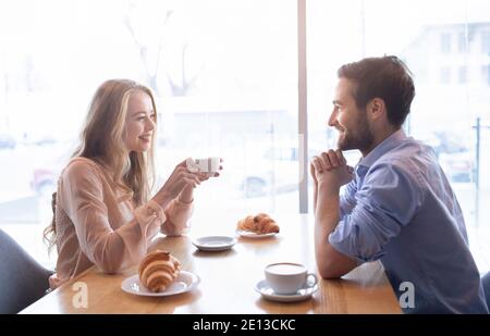 Liebevolles junges Paar beim gemeinsamen Brunch in der Cafeteria, beim freundlichen Gespräch am Fenster, beim Kaffeetrinken Stockfoto
