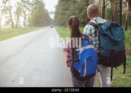 Rückansicht Aufnahme eines gemischten Paares mit Rucksäcken, die auf einer Landstraße im Wald trampeln, Kopierraum Stockfoto