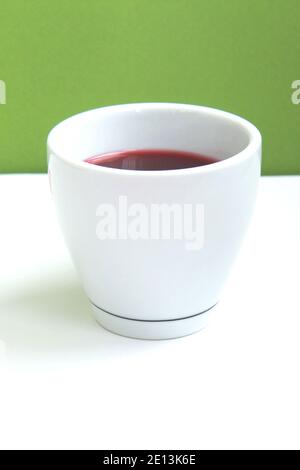 Roter Hibiskustee in einer weißen Tasse auf grünem Hintergrund. Seitenansicht Stockfoto