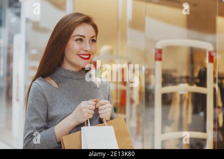 Schöne glückliche junge Frau, die gerne im Einkaufszentrum einkaufen, Taschen mit Kauf tragen, freudig wegschauen, Platz kopieren Stockfoto