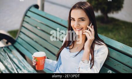 Obere Ansicht Foto von einer charmanten Dame am Telefon sprechen Und einen Kaffee trinken, der auf der Bank mit einem sitzt Notebook Stockfoto