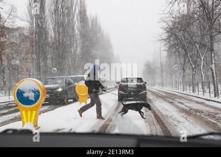 Kiew, Ukraine, 23. Dezember 2020, Fußgänger mit einem Hund Kreuzung Straße bei extremen schlechten Wetterbedingungen mit starkem Schneefall Stockfoto