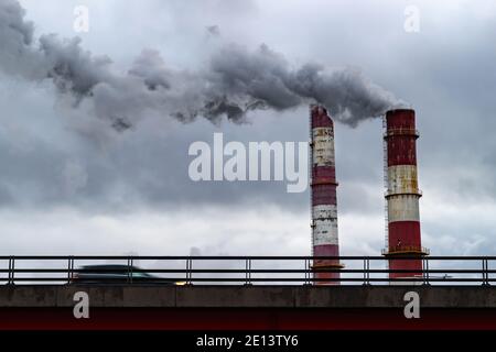 Dunkle giftige Rauchwolken, die über dem Autoverkehr aus dem Fabrikschornstein kommen. Luftverschmutzung und Erderwärmung durch altes Industriekraftwerk Stockfoto