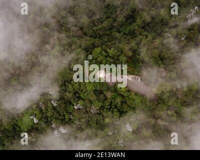 Blick von oben durch Wolken auf grünen Wald und Straße. Stockfoto