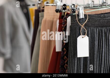 Kleidung auf Kleiderbügeln mit leeren Papieretiketten Stockfoto