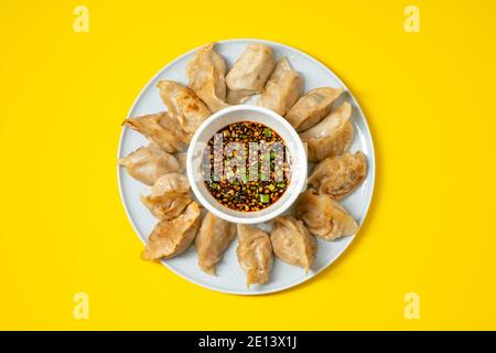 Gebratene Gyoza-Stil Knödel in einem Teller mit würziger Sojasauce auf gelbem Hintergrund. Asiatische Speisen zum Mitnehmen. Stockfoto
