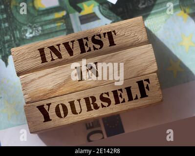 Investieren Sie in sich selbst, Phrase geschrieben auf Holzblöcke stehen auf 100 Euro-Scheine. Soft Skills and Achievements Konzept. Individuelle Einsparungen und Investitionen Stockfoto