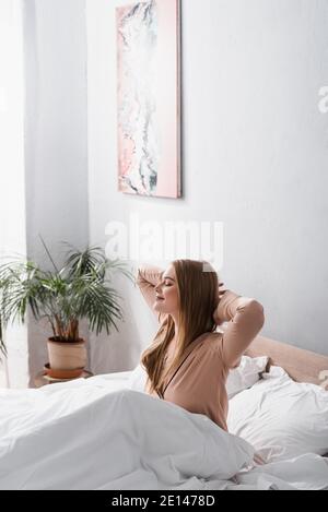 Wach und fröhlich Frau in Seide Pyjamas Stretching im Bett Stockfoto