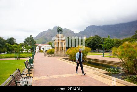 Gärten - Kapstadt, Südafrika - 23/11/2020 Gärten an einem bewölkten Tag. Pferdestatue, Grün und wolkenbedeckten Berg. Mann in Gesichtsmaske, der vorbei geht Stockfoto