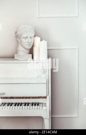 Weißes Klavier mit offenem Deckel auf weißem Hintergrund. Weiße Gipsstatue. Weißes Innenraumkonzept Stockfoto