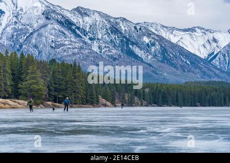 Touristen, die Eislaufen in Johnson Lake gefrorenen Wasseroberfläche im Winter. Schneebedeckter Berg im Hintergrund. Banff National Park Stockfoto