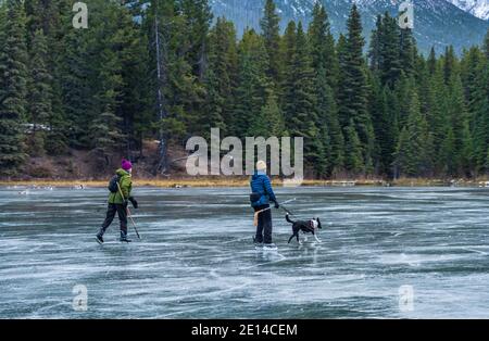 Touristen, die Eislaufen in Johnson Lake gefrorenen Wasseroberfläche im Winter. Schneebedeckter Berg im Hintergrund. Banff National Park Stockfoto