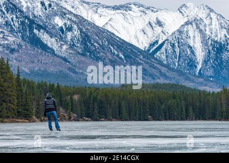 Touristen, die Eislaufen in Johnson Lake gefrorenen Wasseroberfläche im Winter. Schneebedeckter Berg im Hintergrund. Banff National Park Stockfoto