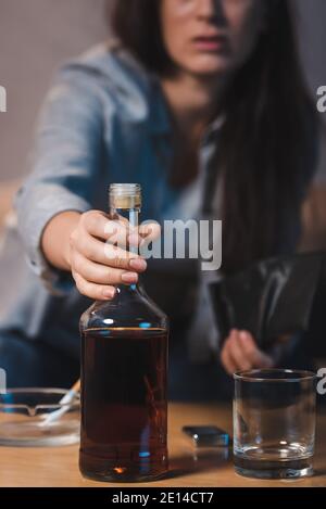 Teilansicht einer alkoholischen Frau, die eine Flasche Whiskey vom Tisch nimmt, verschwommener Hintergrund Stockfoto