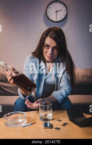 Alkoholsüchtige Frau, die die Kamera anschaut, während sie eine Flasche Whiskey hält Stockfoto