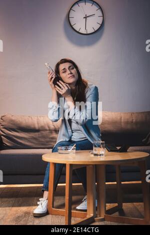 Verärgert, betrunkene Frau hält Flasche Wein in der Nähe des Kopfes, während zu Hause allein sitzen Stockfoto