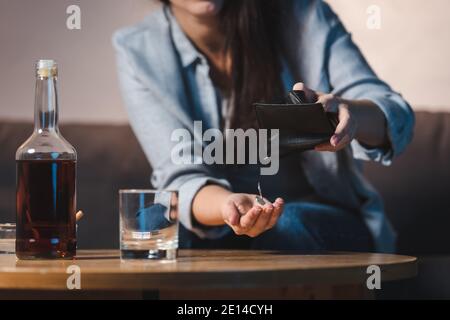 Teilansicht der Frau, die Münzen aus der Brieftasche neben einer Flasche Whiskey auf dem Tisch nimmt, verschwommener Hintergrund Stockfoto