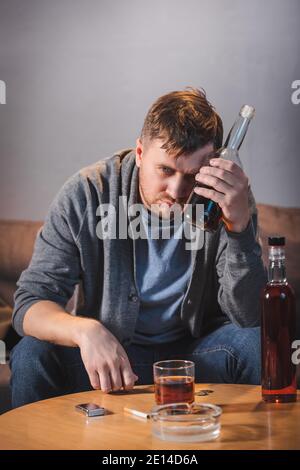 Betrunkener, alkoholsüchtiger Mann, der zu Hause eine Flasche Whiskey hält Stockfoto