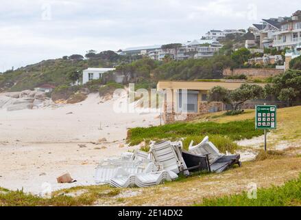 Camps Bay- Kapstadt, Südafrika - 23/11/2020 gestapelte weiße Plastikliegen am Strand von Camps Bay. Grasbewachsene Steigung im Vordergrund. Stockfoto