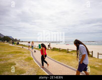 Camps Bay - Kapstadt, Südafrika - 23/11/2020 Paar zu Fuß über Camps Bay Promenade. Frau trägt leuchtend rote Spitze, Mann mit Dreadlocks. Stockfoto