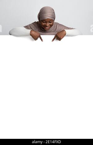 Aktivieren Sie Diese Option. Afrikanische muslimische Dame in Hijab zeigt auf weiße Werbetafel Stockfoto