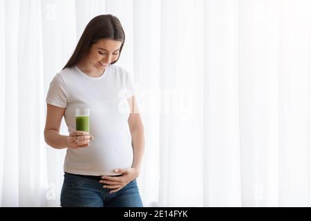Glückliche junge schwangere Frau trinken grünen Gemüsesaft oder Smoothie Zu Hause Stockfoto