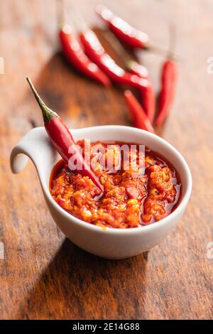 Rote Chili-Paste und Chili-Pfeffer in Schüssel auf Holztisch. Stockfoto