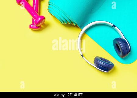 Flat Lay Sport- und Fitnessgeräte, rosa Kurzhanteln, Kopfhörer und Minze Yoga Matte auf gelbem Hintergrund. Ansicht von oben mit Platz für Text Stockfoto