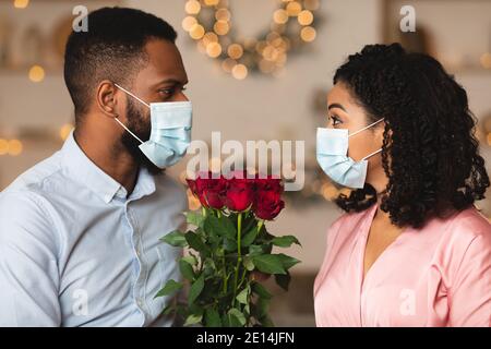 Schwarzes Paar in medizinischen Gesichtsmasken mit Datum, halten Rosen Stockfoto