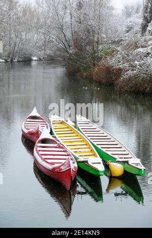 Bunte Paddelboote im Winterschlaf auf dem Fluss mit Schnee Hintergrund und Schneeflocken Stockfoto