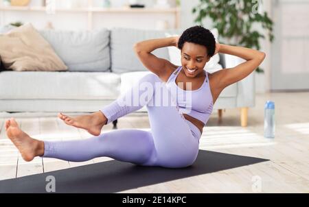 Sport beim Lockdown. Schöne schwarze Dame, die Heimfitness auf Yogamatte tut und ihren ganzen Körper ausarbeitet Stockfoto