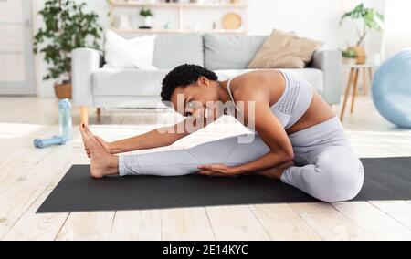 Übungen zur Flexibilität. Sportliche junge Frau, die Yoga auf der Matte macht und ihre Beine während des Heimtrainings streckt Stockfoto