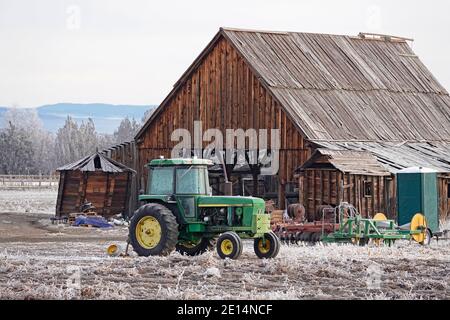 Ein Oldtimer-Traktor sitzt im Dezember vor einer noch älteren Holzscheune auf einer kleinen Farm in Tumalo, Oregon. Stockfoto
