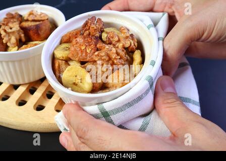 Hand hält eine beheizte Schüssel mit frisch gebackenem Bananenbrot Pudding mit Walnuss Platzierung auf Holz Breadboard Stockfoto
