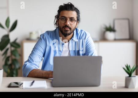 Portrait Des Hübschen Jungen Arabischen Freiberuflers, Der Am Schreibtisch Sitzt Mit Laptop Stockfoto