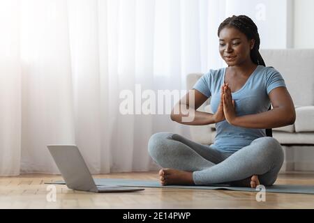 Yoga Zu Hause. Ruhige Schwarze Dame Meditiert Vor Dem Laptop Stockfoto