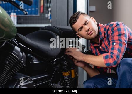 Reparaturman im karierten Hemd, das Diagnose des Motorrads in der Werkstatt macht Stockfoto
