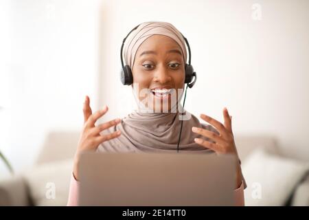 Remote-Arbeit, Kommunikation, Bildung. Glückliche muslimische Dame in Hijab trägt Headset, mit Videoanruf auf Laptop zu Hause Stockfoto