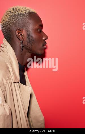 Seitenansicht auf brutal zuversichtlich afrikanischen Mann in trendigen tragen isoliert im Studio mit rotem Hintergrund, modische Kerl posiert, wegschauen. Profil portrai Stockfoto