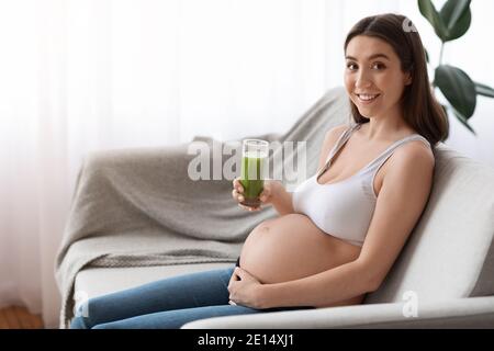 Happy Young Schwangere Frau Mit Glas Grün Smoothie Sitzend Auf Dem Sofa Stockfoto