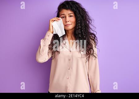 Frau stehen weinend isoliert über lila Hintergrund, verwenden Sie ein Taschentuch, um ihr Gesicht zu wischen Stockfoto