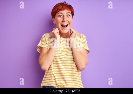 Frau mit roten kurzen Haaren Spaß haben, lachen an Kamera isoliert über lila Hintergrund, junge Frau in Freizeitkleidung genießen das Leben Stockfoto