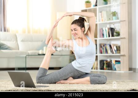 Ganzkörper-Porträt einer glücklichen Frau zu Hause beobachten Yoga-Tutorial online auf Laptop Stockfoto